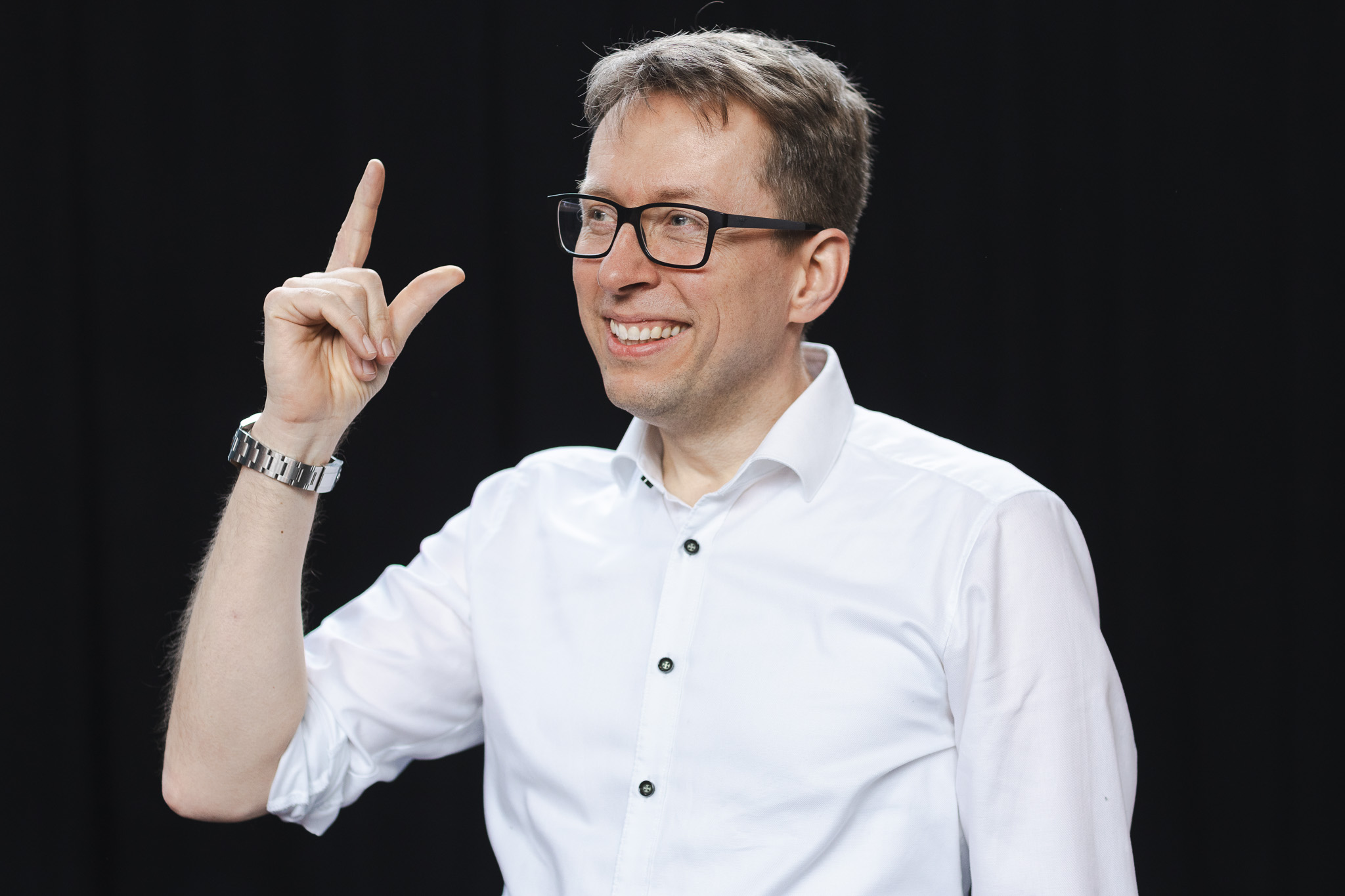 Daniel Schwenger smiling and gesturing in front of a black studio backdrop