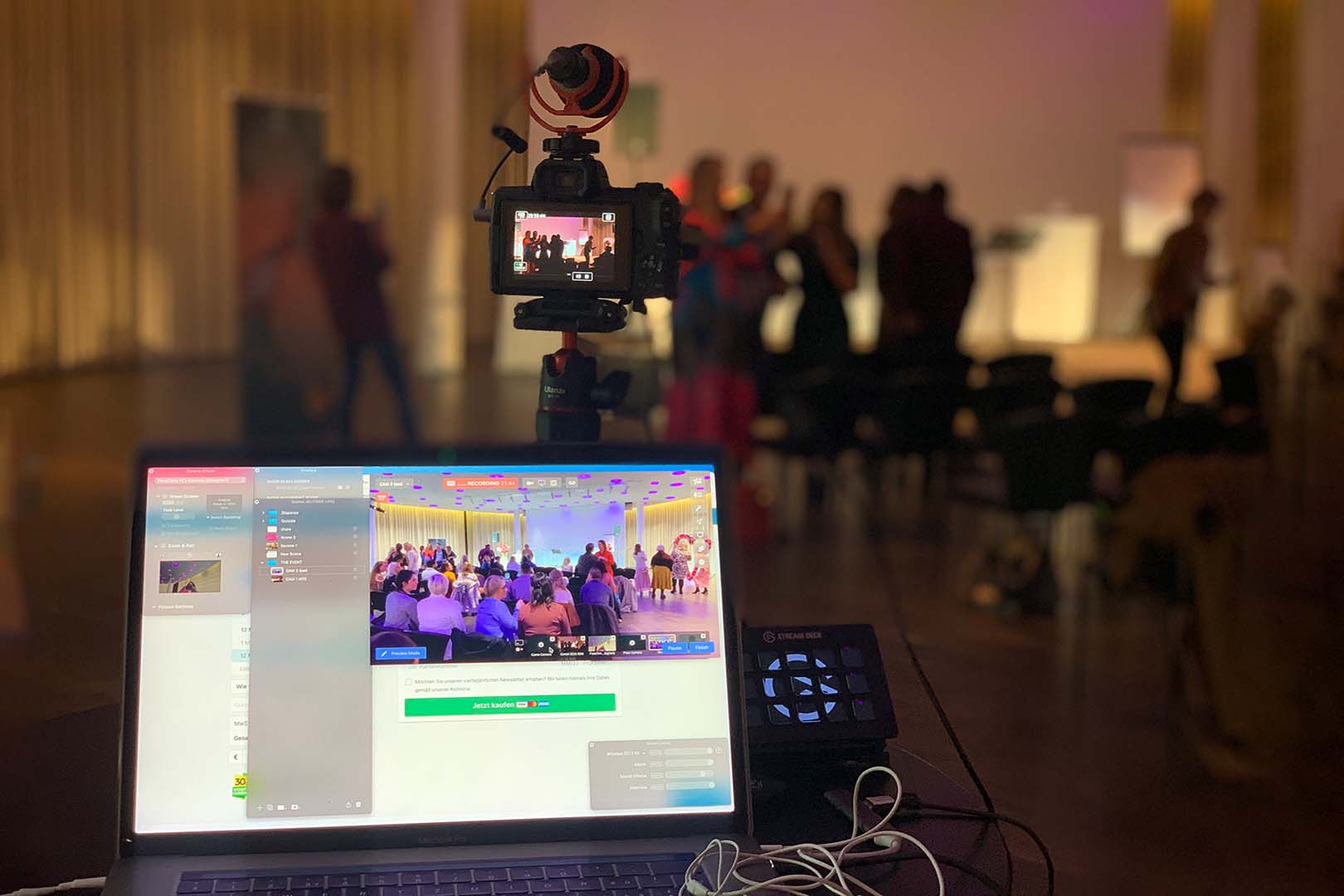 Camera on a tripod and streaming laptop in front of a live event audience